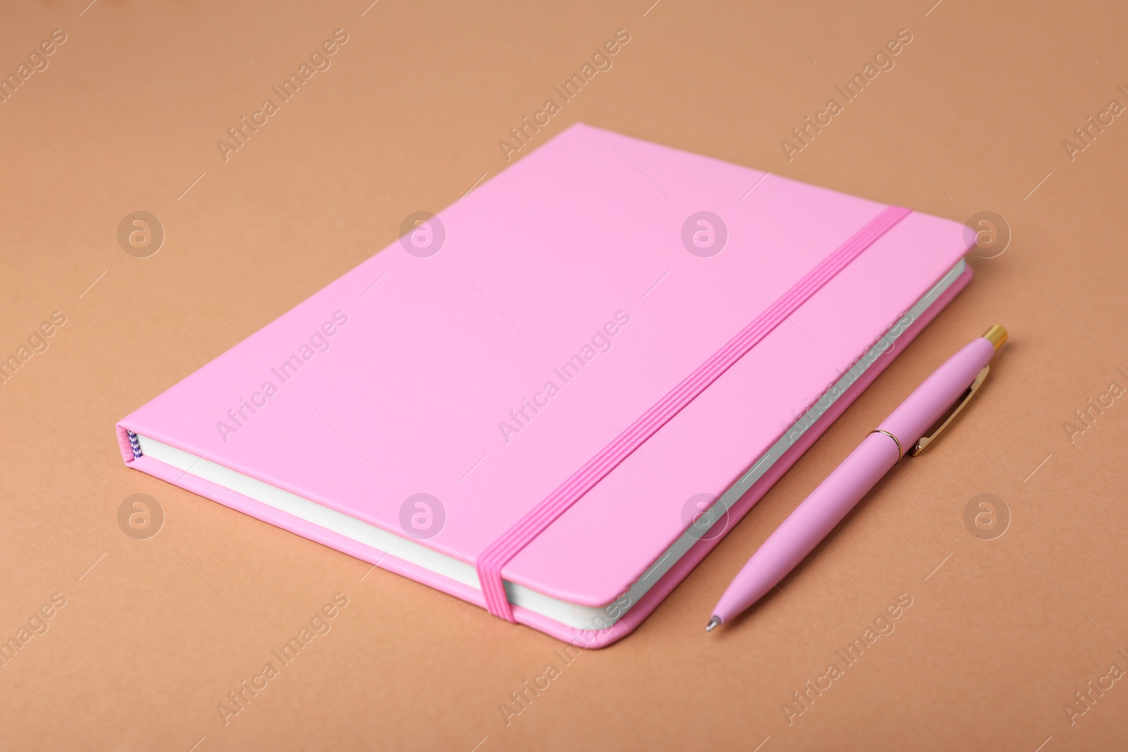 Photo of Closed pink notebook and pen on light brown background