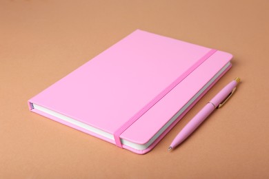 Closed pink notebook and pen on light brown background