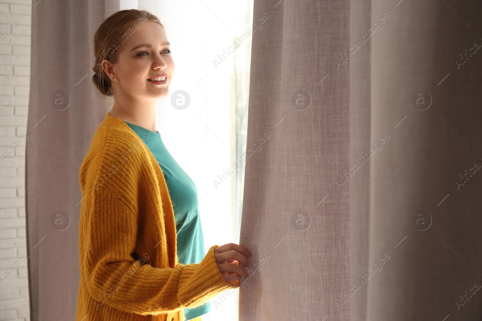 Photo of Woman near window with beautiful curtains at home. Space for text