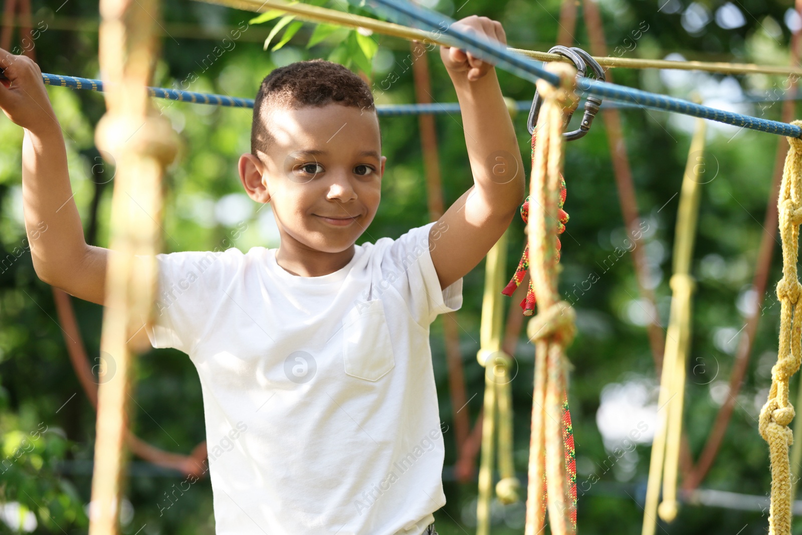 Photo of Little African-American boy climbing in adventure park. Summer camp