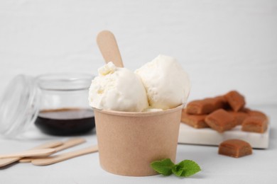 Photo of Delicious vanilla ice cream in paper cup on white wooden table