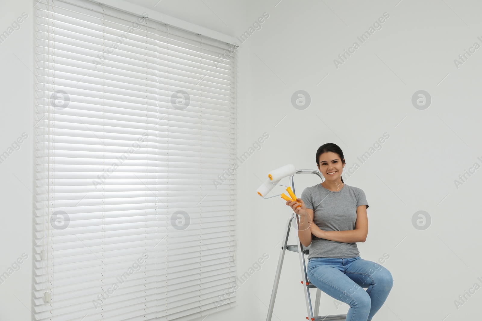 Photo of Woman sitting on metallic folding ladder indoors, space for text