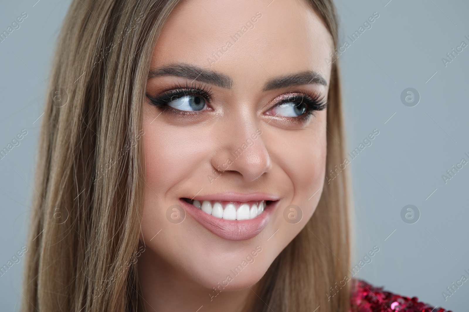 Photo of Happy woman with makeup on grey background, closeup