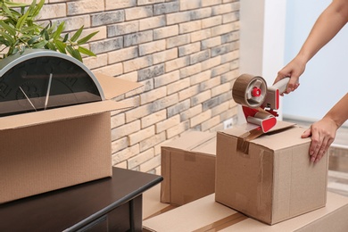 Woman packing carton box indoors, closeup. Moving day