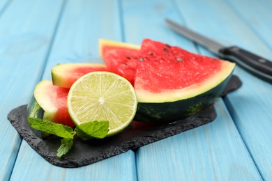 Photo of Slate board with cut watermelon and lime on light blue wooden table