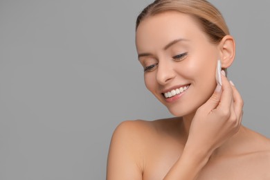 Smiling woman removing makeup with cotton pad on grey background. Space for text