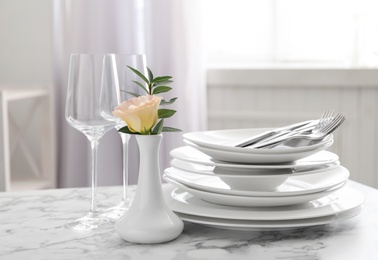 Photo of Set of clean dishes and vase with flower on white marble table