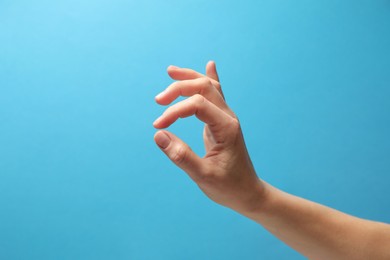 Woman holding something in hand on light blue background, closeup