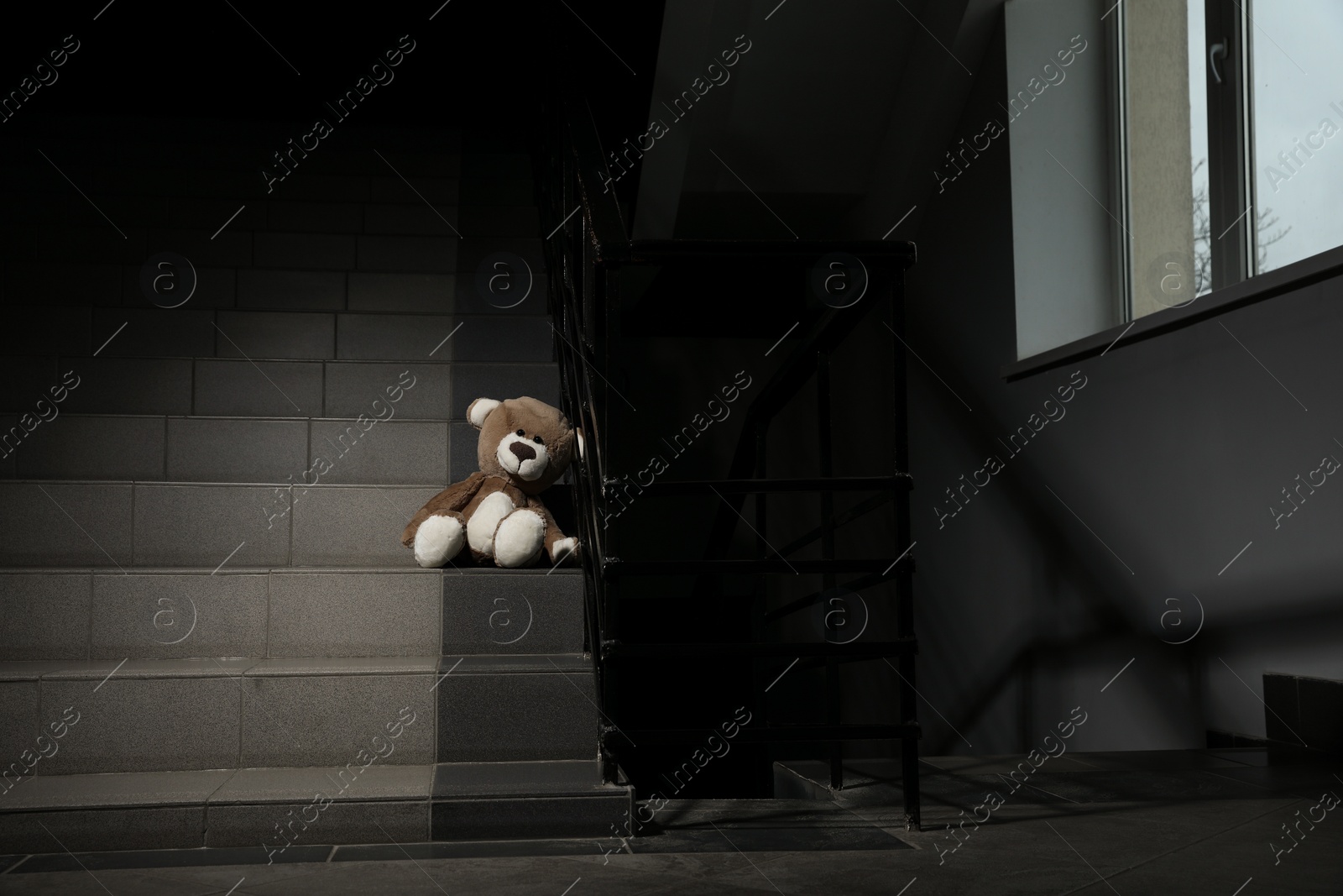 Photo of Lonely teddy bear on staircase near metal railing indoors
