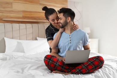 Happy couple in pajamas with laptop on bed at home