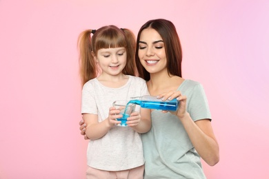 Photo of Little girl and her mother with mouthwash on color background. Teeth and oral care