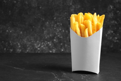 Photo of Delicious french fries in paper box on black table, space for text