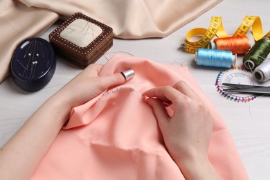 Woman with sewing needle and thread embroidering on cloth at white wooden table, closeup