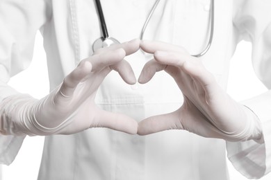 Photo of Doctor in medical gloves making heart with her hands on white background, closeup