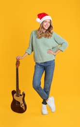 Photo of Young woman in Santa hat with electric guitar on yellow background. Christmas music
