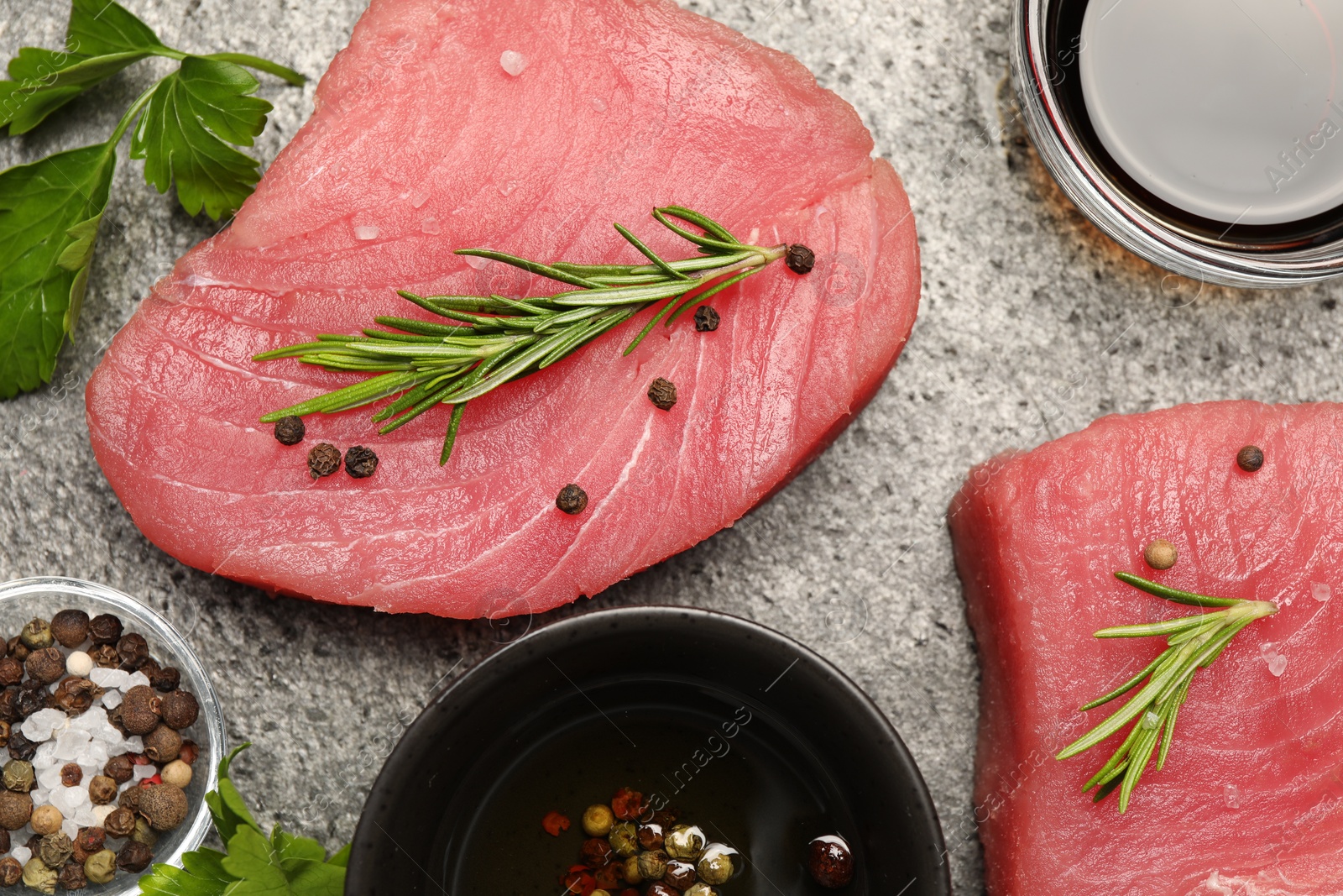 Photo of Raw tuna fillets with herbs and spices on gray table, flat lay