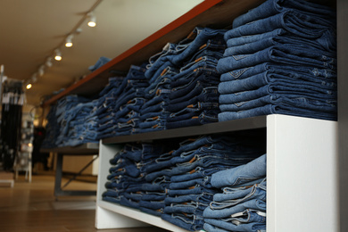 Photo of Collection of stylish jeans on shelves in shop