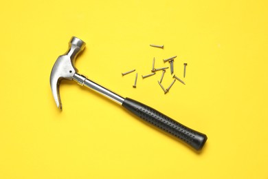 Photo of Hammer and metal nails on yellow background, top view