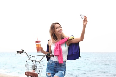 Photo of Attractive woman taking selfie near bicycle on sea coast