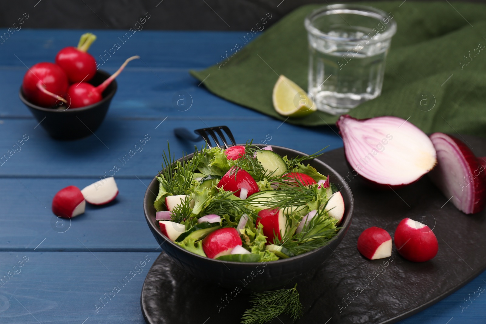 Photo of Tasty salad with radish in bowl on blue wooden table