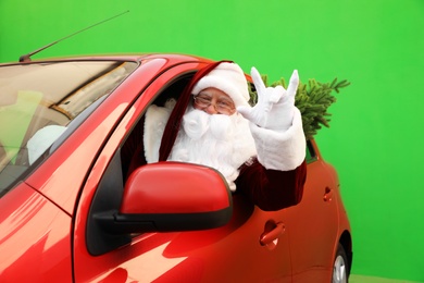 Authentic Santa Claus with fir tree driving car against green background