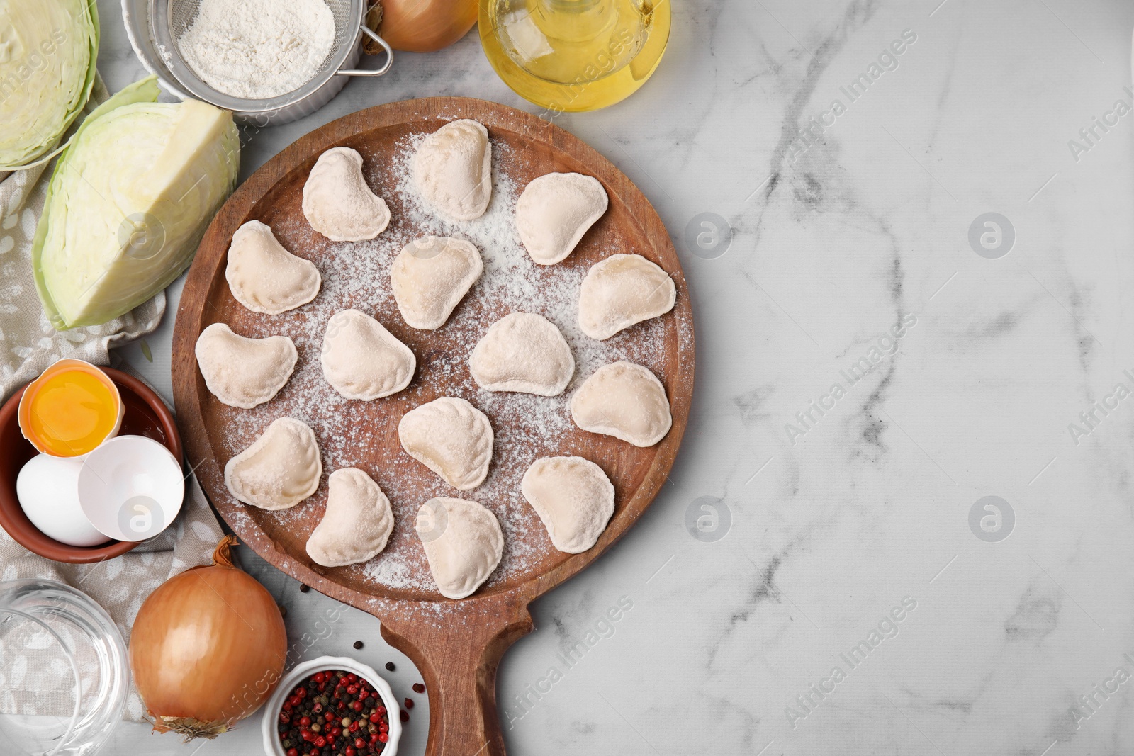 Photo of Raw dumplings (varenyky) with tasty filling, cut cabbages and egg yolk on white marble table, flat lay. Space for text