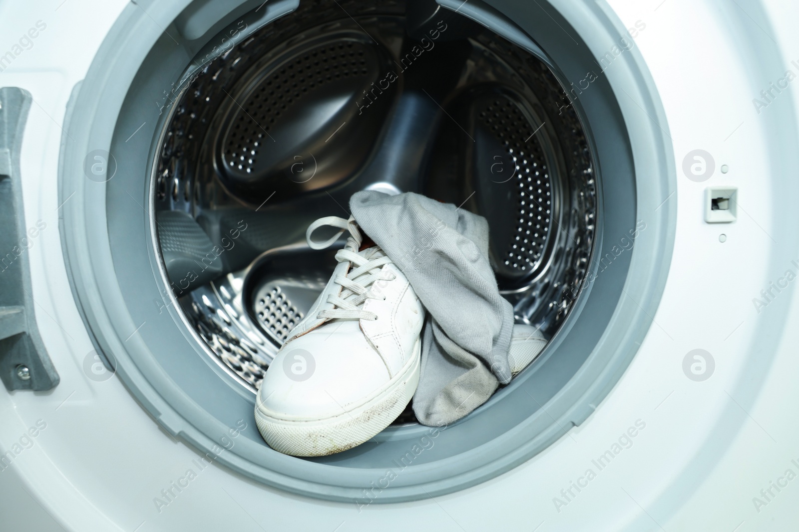 Photo of Sneakers with dirty socks in washing machine, closeup