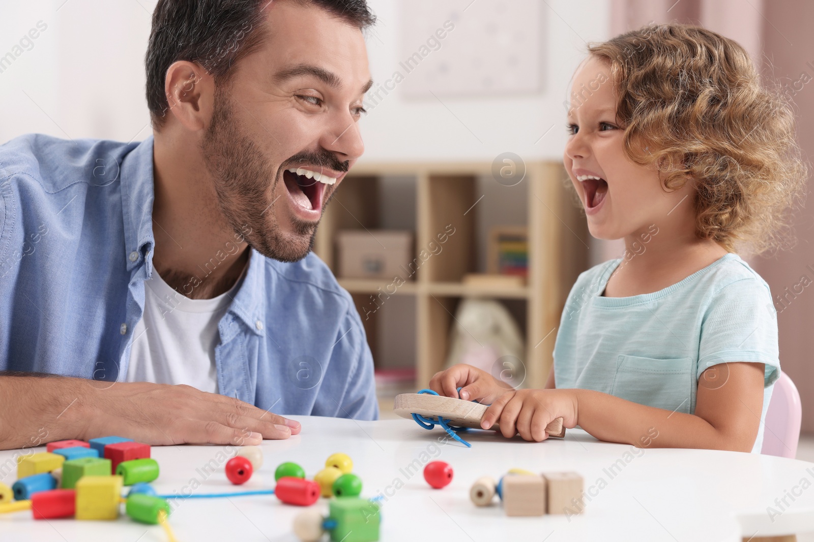 Photo of Motor skills development. Father and daughter playing with wooden lacing toy at table indoors