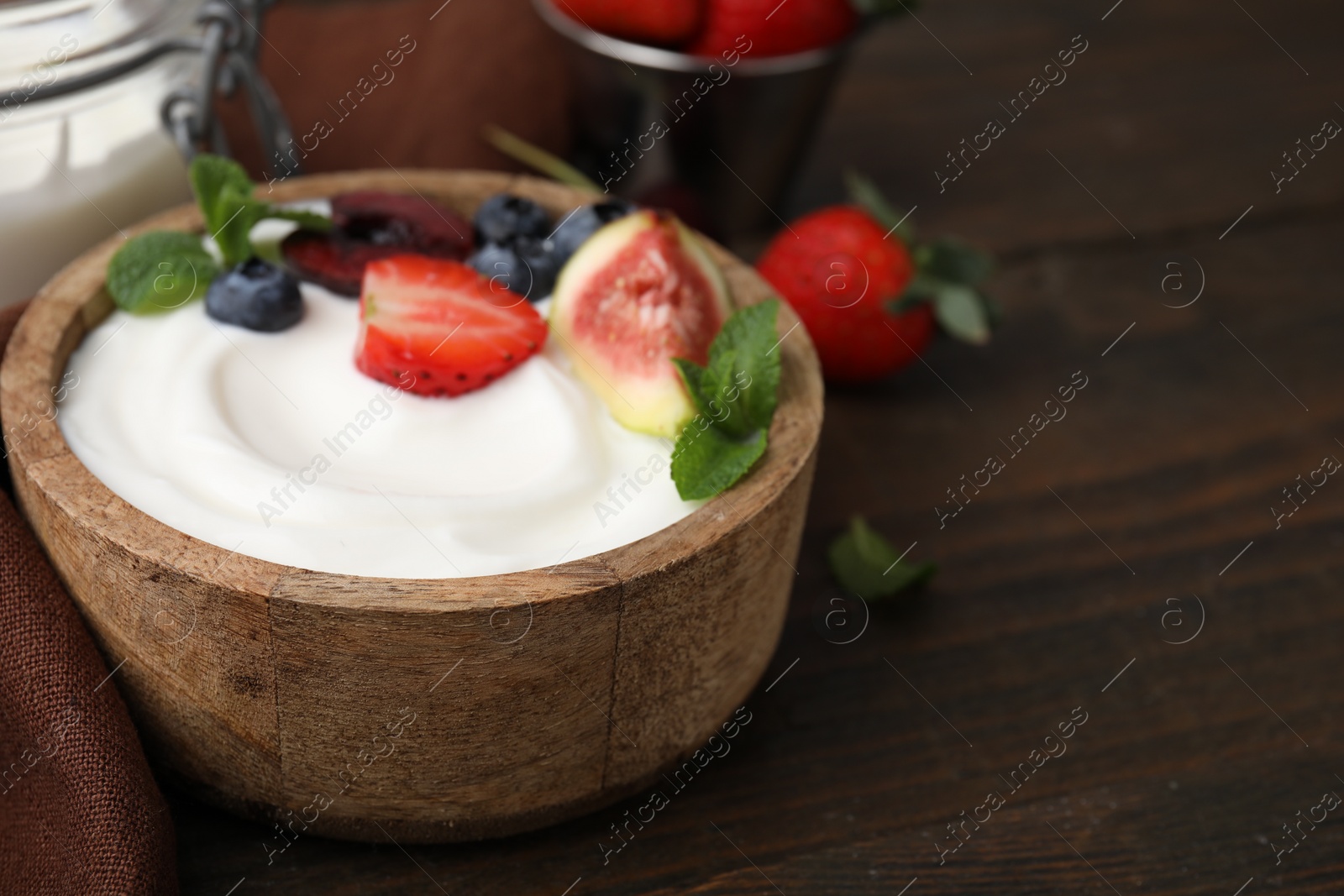 Photo of Bowl with yogurt, berries, fruits and mint on wooden table, closeup. Space for text