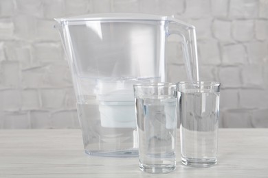 Photo of Filter jug and glasses with purified water on white table indoors