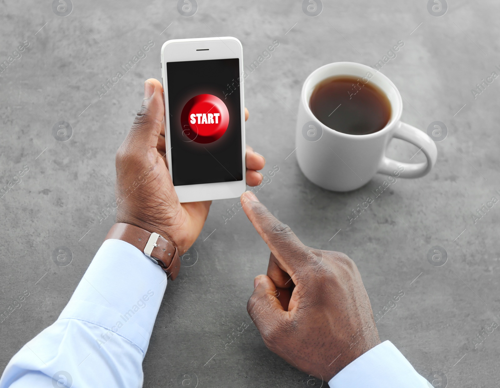 Image of African-American man pointing at start icon on smartphone at table, closeup