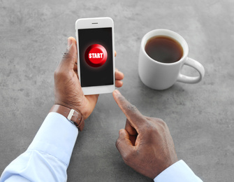 Image of African-American man pointing at start icon on smartphone at table, closeup