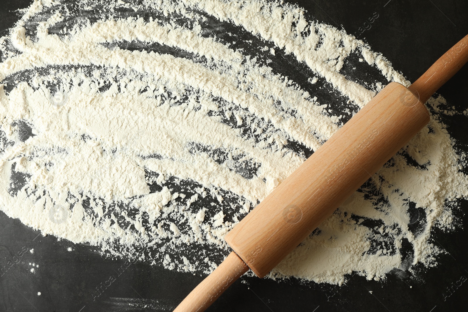 Photo of Scattered flour and rolling pin on black table, top view