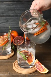 Photo of Woman pouring refreshing drink with sicilian orange from jug into glass at wooden table, closeup