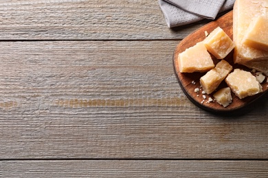 Photo of Pieces of delicious parmesan cheese on wooden table, top view. Space for text