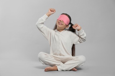 Photo of Cute girl in white pajamas with pink sleep mask on light grey background