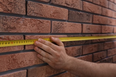 Man measuring brick wall, closeup. Construction tool