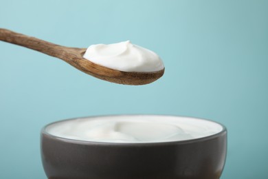 Photo of Eating delicious natural yogurt on light blue background, closeup