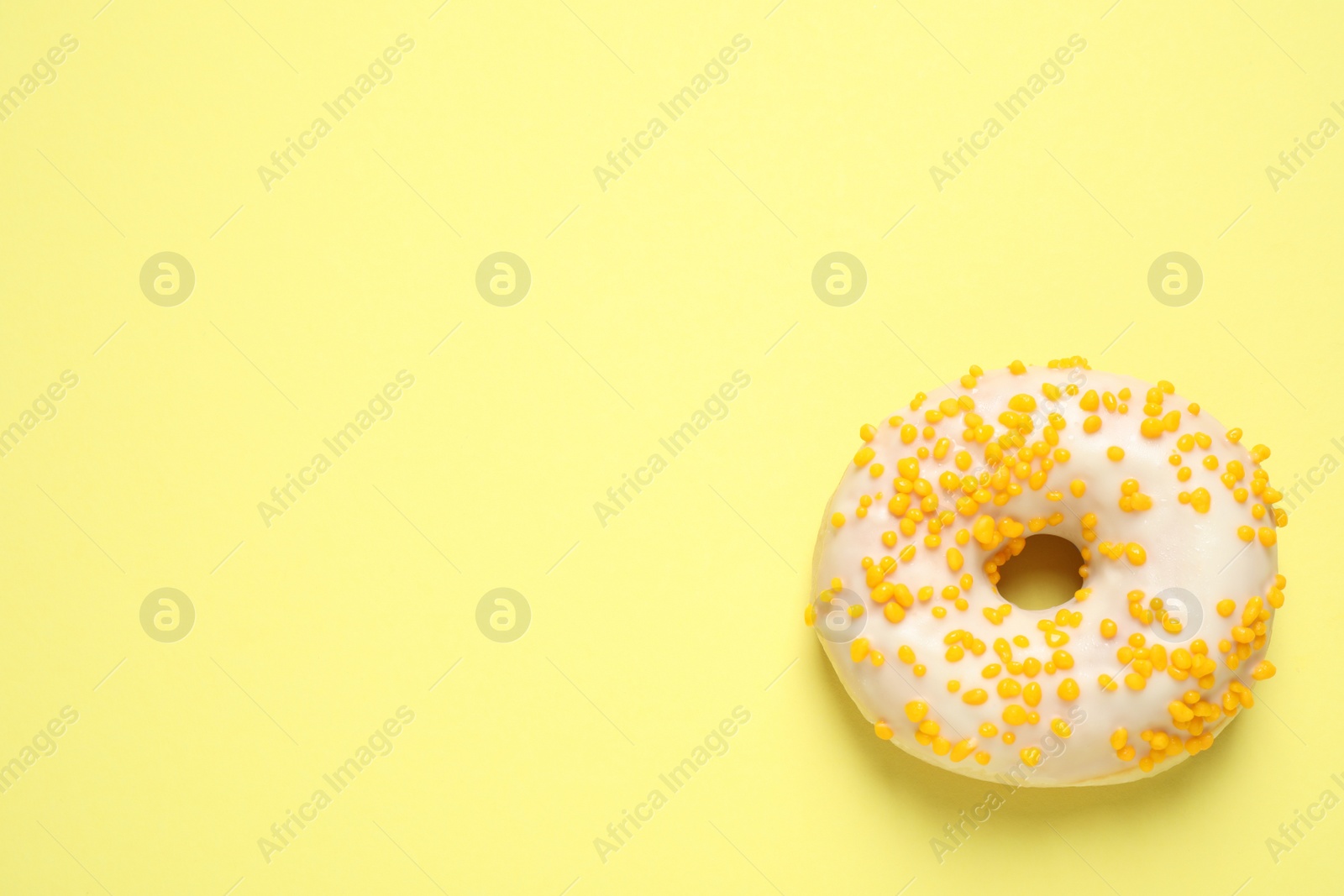 Photo of Delicious glazed donut on yellow background, top view. Space for text