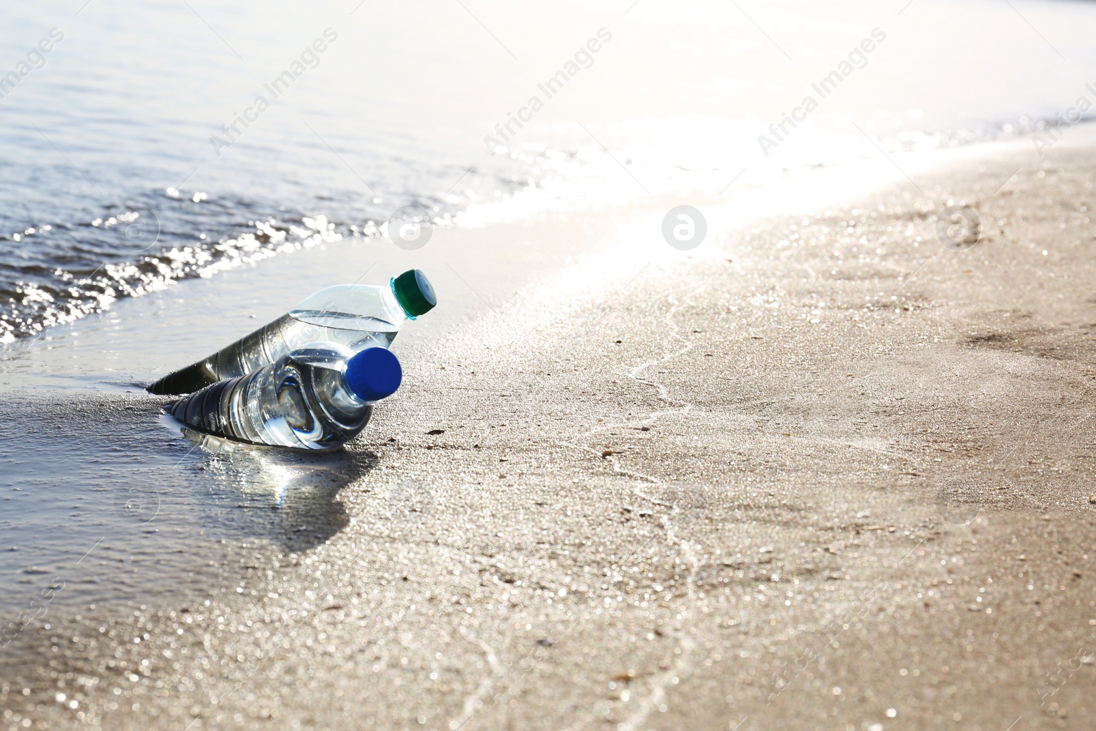 Photo of Bottles of refreshing drink in wet sand near sea on hot summer day, space for text