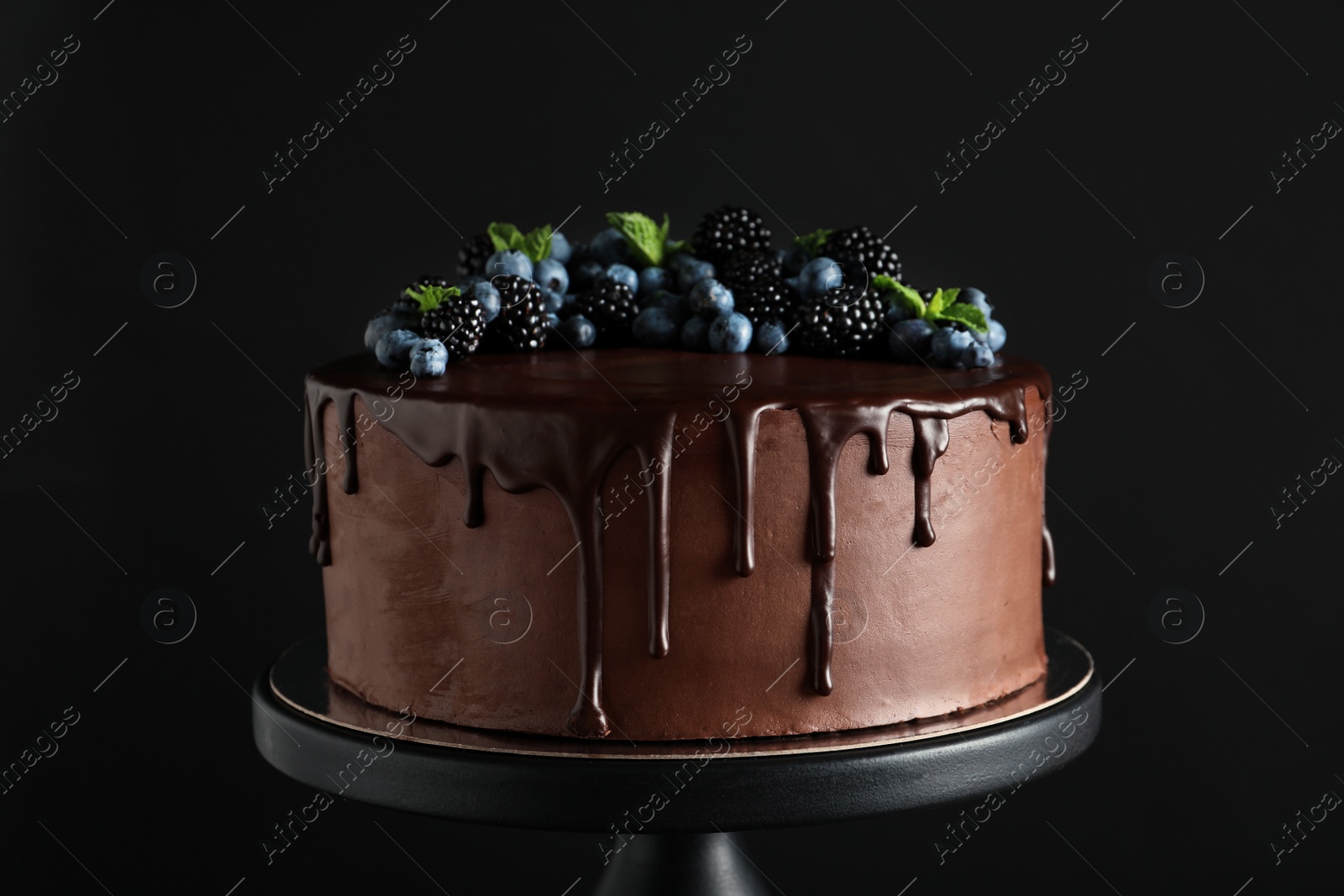 Photo of Fresh delicious homemade chocolate cake with berries on dessert stand against dark background