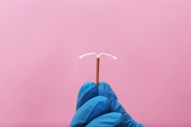Photo of Doctor holding T-shaped intrauterine birth control device on pink background, closeup