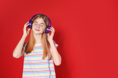 Teenage girl enjoying music in headphones on color background. Space for text