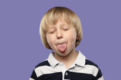 Photo of Cute little boy showing his tongue on purple background