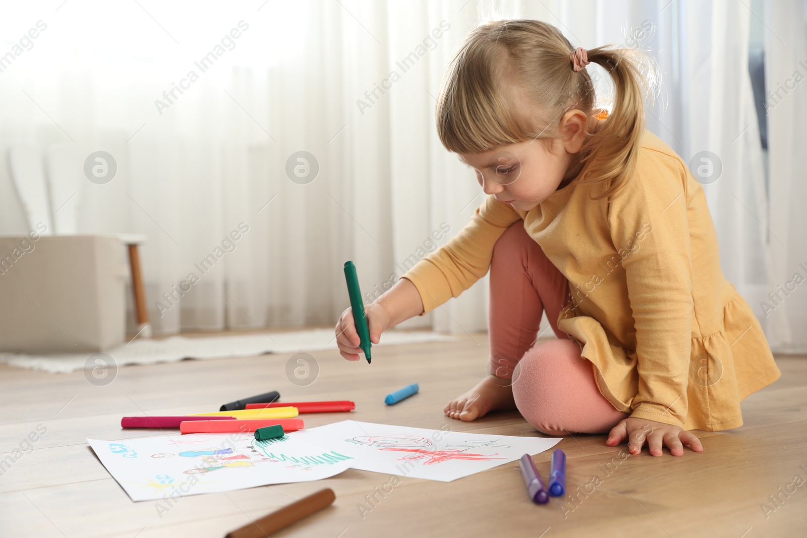 Photo of Cute little girl drawing with marker on floor indoors. Child`s art