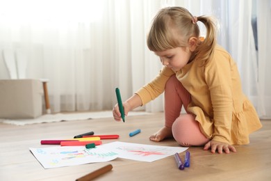 Photo of Cute little girl drawing with marker on floor indoors. Child`s art