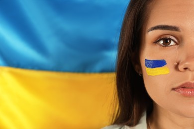 Photo of Young woman with face paint near Ukrainian flag, closeup. Space for text