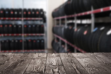 Empty wooden surface and blurred view of car tires in auto store, closeup. Space for text 