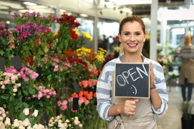 Photo of Female florist holding sign "OPEN" in flower shop
