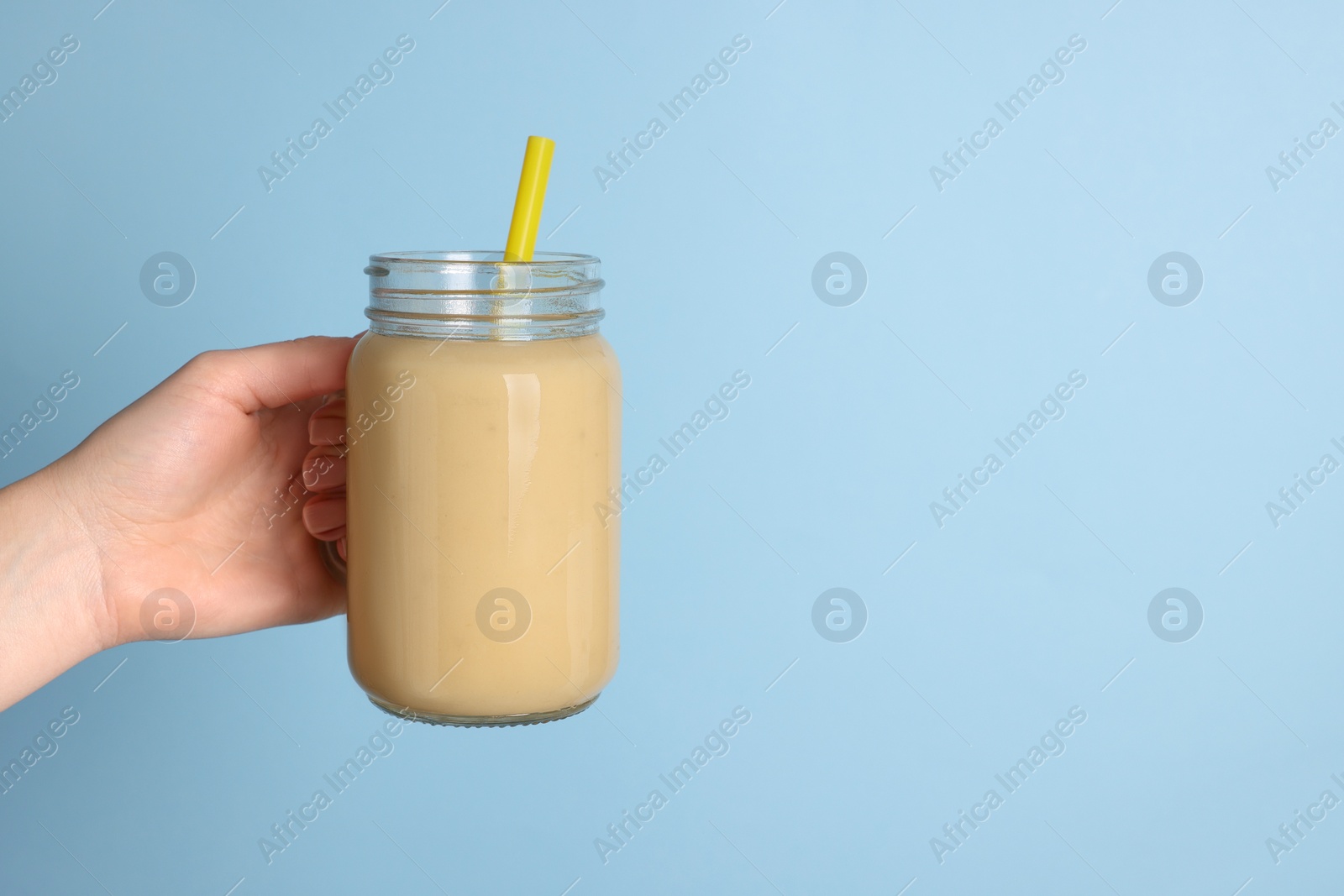 Photo of Woman holding mason jar with tasty smoothie and straw on light blue background, closeup. Space for text